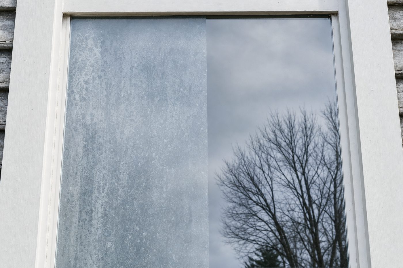 A window pane divided down the middle: cloudy white hard water mineral scale on one side, clear reflective glass on the other